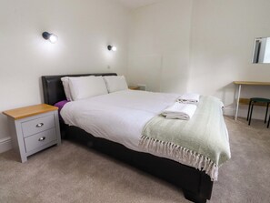 A neatly made bed with white linens, a bedside table with drawers, a small desk with a chair, and two wall-mounted light fixtures. - 6 Hazel Moor (Blackburn)