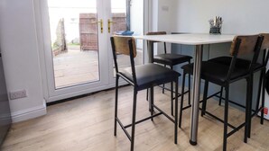 A dining area with a table and four chairs, a sliding glass door leading outside, and a small side table with utensils. - 6 Hazel Moor (Blackburn)