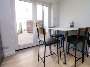 A dining area with a table and four chairs, a sliding glass door leading outside, and a small side table with utensils. - 6 Hazel Moor (Blackburn)