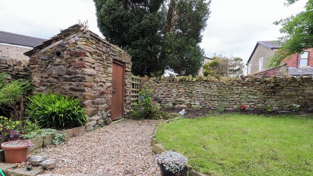 A stone building with a wooden door, surrounded by a stone wall and a grassy area. - 6 Hazel Moor (Blackburn)