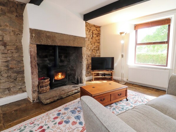 A cozy living room with a stone fireplace, a television on a wooden stand, a sofa, and a floor lamp. - 6 Hazel Moor (Blackburn)