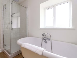 A bathroom with a glass-enclosed shower, a freestanding bathtub, and a window above the bathtub.