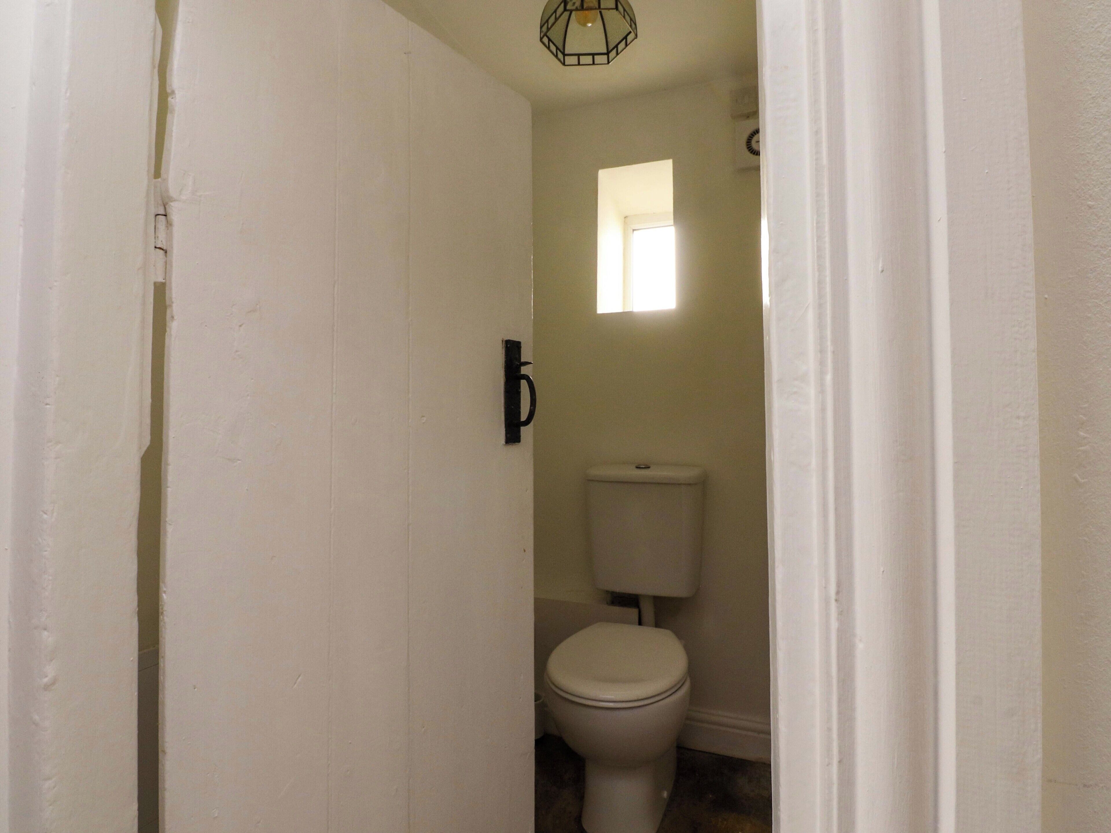 A narrow hallway leading to a bathroom with a toilet, a small window, and a door with a letter 'b' on it.