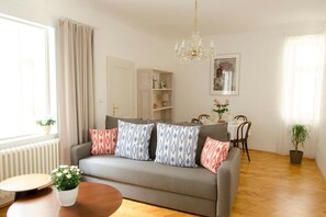 Ein Wohnzimmer mit einer Couch, einem Esstisch, einer Chandelier und einer Zimmerpflanze.