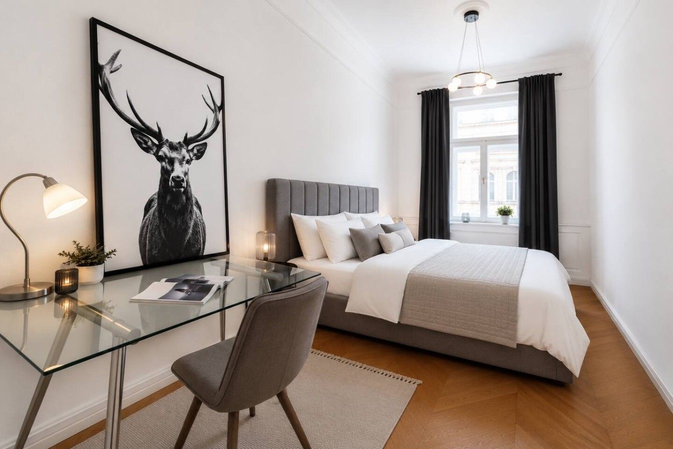 A modern bedroom with a glass desk, a bed with a grey headboard, and a large window with curtains.