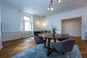 Ein modernes Zimmer mit einem runden Holztisch, grauen Stühlen, einer Topfpflanze und einem großen Fenster.