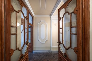 A hallway with two wooden doors with glass panels, a decorative wall panel, and a brick floor. - Golden Prague Residence – Jáchymova Street (Prague)