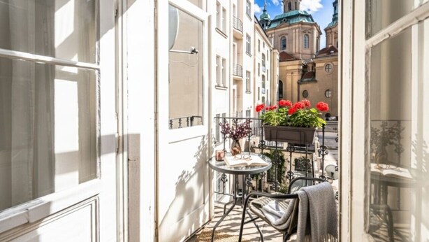 Un petit balcon extérieur, avec une table, des chaises et des plantes en pot.