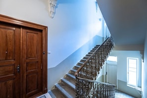 A wooden door, a staircase with ornate metal railings, and a window allowing natural light. - Golden Prague Residence – Jáchymova Street (Prague)