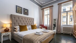 Une chambre d’hôtel avec un grand lit, une table de chevet avec une lampe, un fauteuil rouge et une fenêtre avec des rideaux.