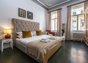 A hotel room with a large bed, a nightstand with a lamp, a red chair, and a window with curtains. - Golden Prague Residence – Jáchymova Street (Prague)