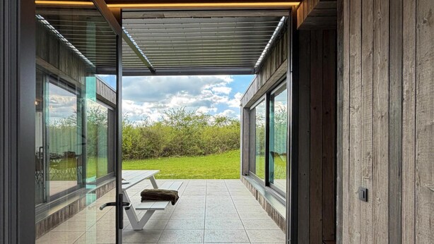 A modern patio with a glass door, a white bench, and a view of a grassy area. - Luxury Design in the Heart of Nature (Somme-Leuze)