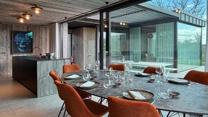 A modern dining area with a large table, orange chairs, and a view of the outdoors. - Luxury Design in the Heart of Nature (Somme-Leuze)