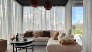 A modern living room with a sectional sofa, a round coffee table, and a view of a garden through large windows. - Luxury Design in the Heart of Nature (Somme-Leuze)