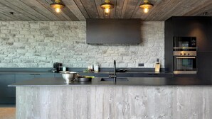 A modern kitchen with a large island, stone wall, and built-in appliances. - Luxury Design in the Heart of Nature (Somme-Leuze)