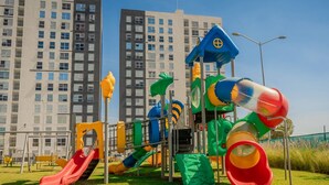 A playground with slides and climbing structures, surrounded by grass and buildings in the background. - Gdl Sky Luxury residence (Zapopan)