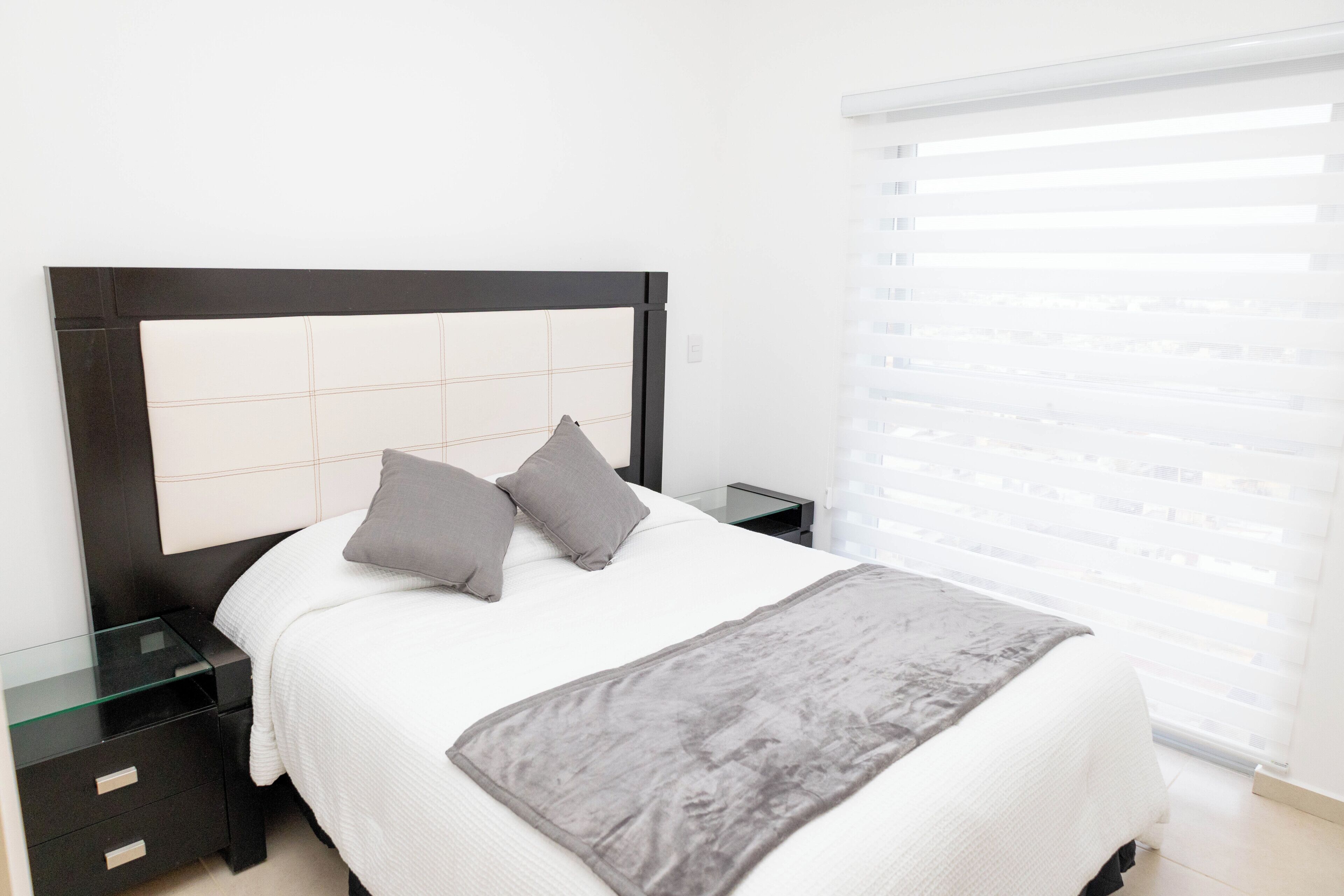 Un dormitorio moderno con una cama, dos mesitas de noche y una ventana con persianas.