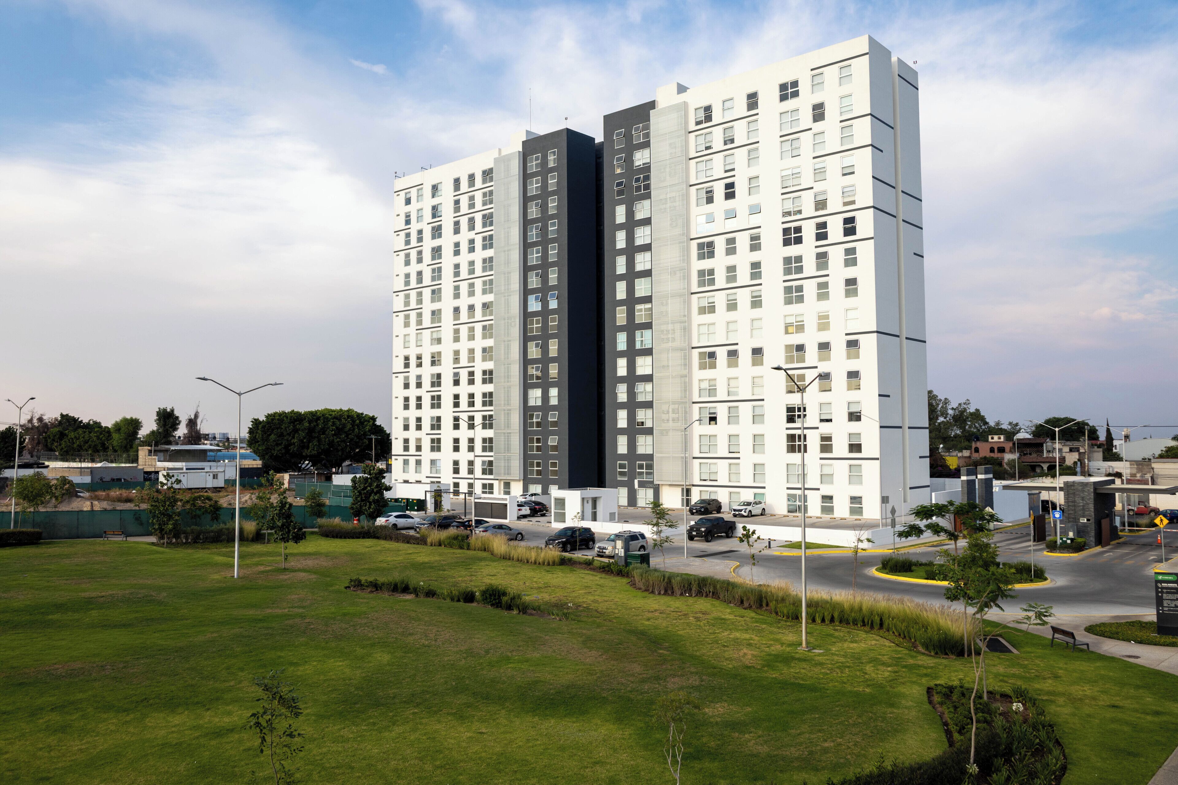 Un edificio alto con varios pisos, rodeado de un área verde bien cuidada y algunos árboles.