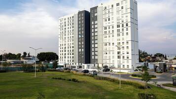 Un edificio alto con varios pisos, rodeado de un área verde bien cuidada y algunos árboles.