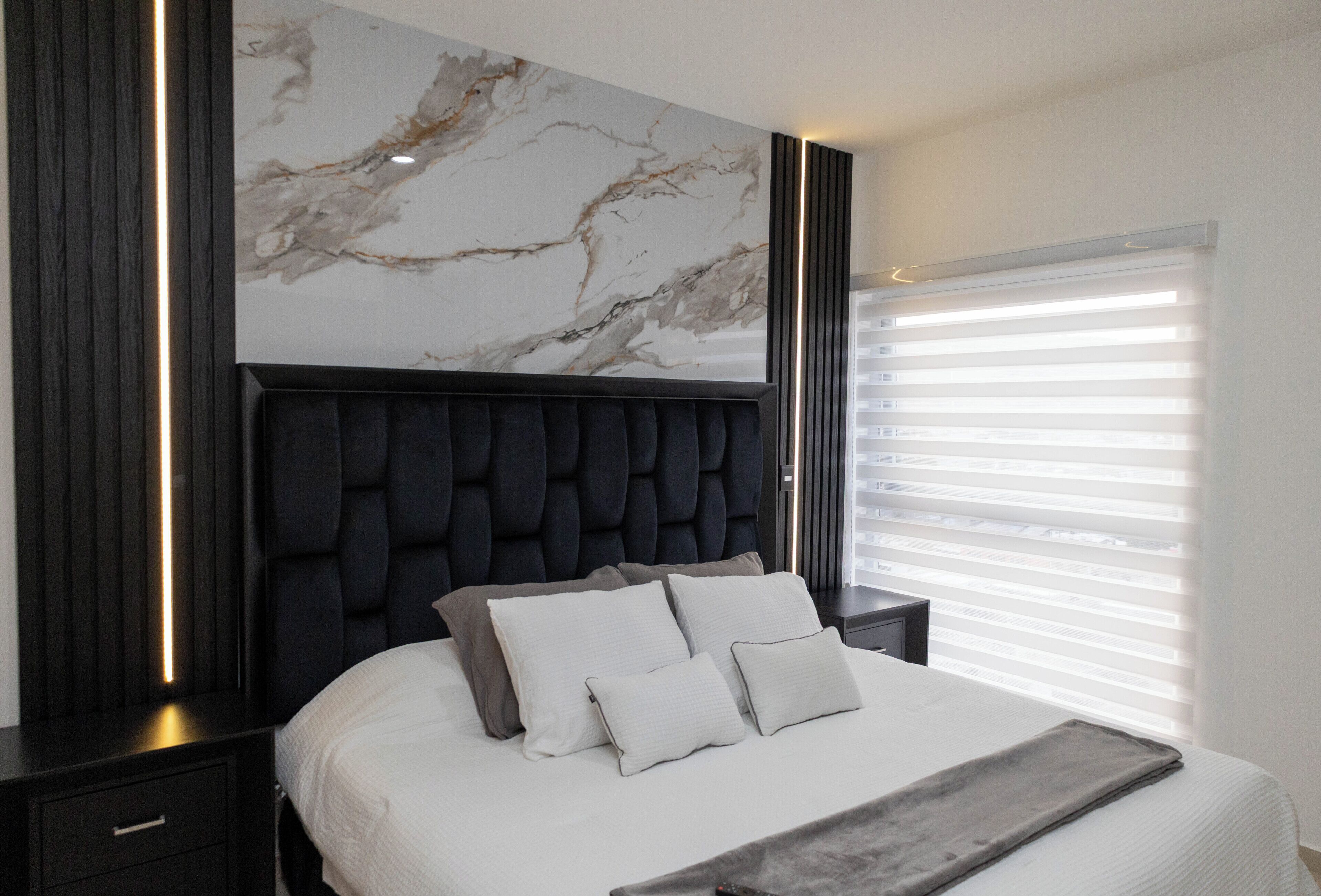 Un dormitorio moderno con cabecera de mármol, una cama grande con ropa de cama blanca y una mesita de noche con lámpara.