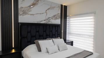 Un dormitorio moderno con cabecera de mármol, una cama grande con ropa de cama blanca y una mesita de noche con lámpara.