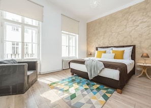 A bedroom with a bed, a sofa, a patterned rug, and a window. - Elegant Two-Bedroom Apartment in New Town (Prague)