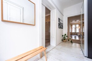 A hallway with a wooden bench, a door leading to a kitchen, and a potted plant. - Elegant Two-Bedroom Apartment in New Town (Prague)