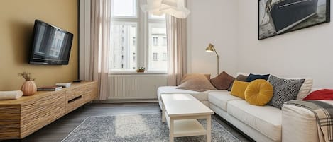 A modern living room with a sofa, a coffee table, a TV, and a window with curtains.