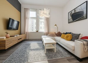 A modern living room with a sofa, a coffee table, a TV, and a large window with curtains. - Elegant Two-Bedroom Apartment in New Town - Revolucni (Prague)