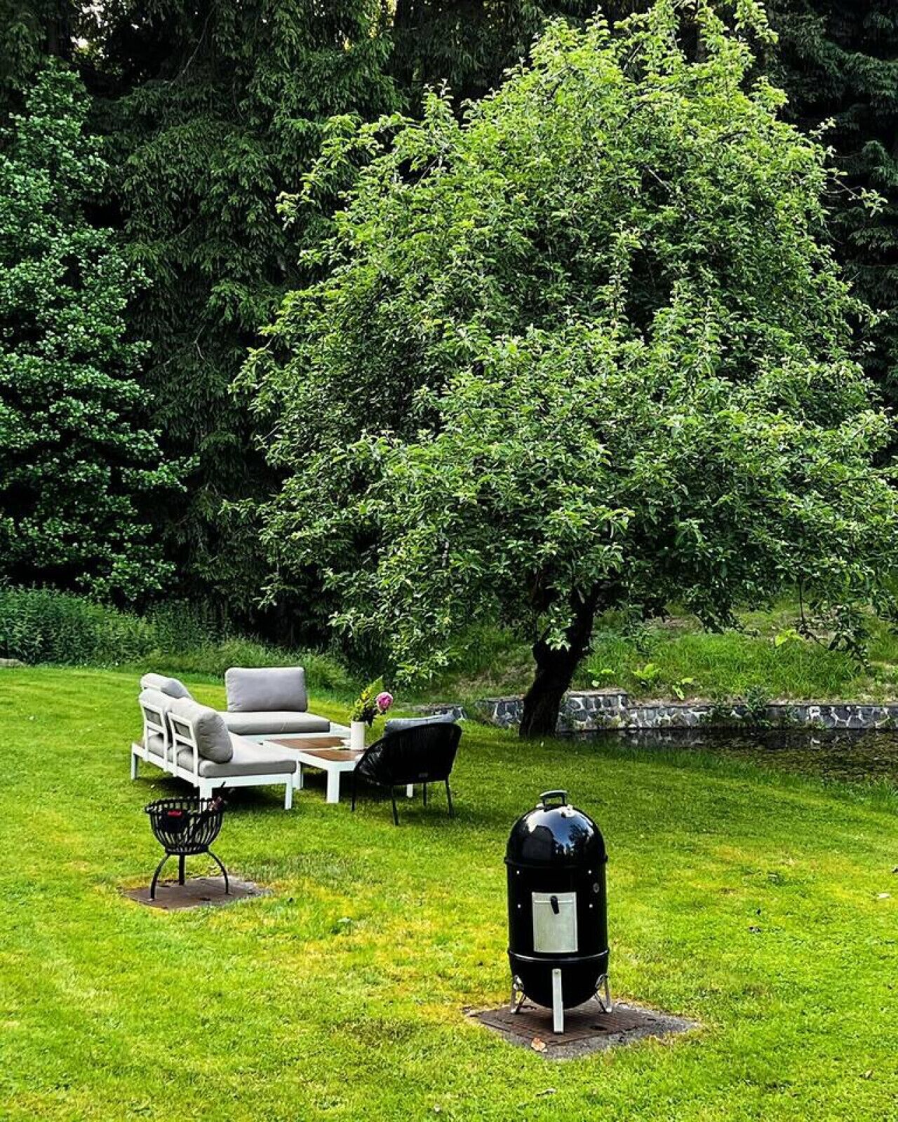 Un espace extérieur verdoyant avec un canapé blanc, une chaise noire et un barbecue.