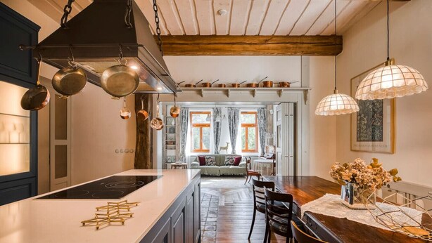 Una cocina moderna con una isla central, ollas de cobre colgadas y un comedor con mesa y sillas de madera.