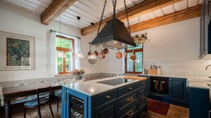 Una cocina con isla central, armarios azules, ollas de cobre colgantes y techo de madera.
