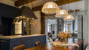 Una cocina con armarios azul oscuro, una isla de madera, ollas de cobre colgantes y lámparas colgantes.
