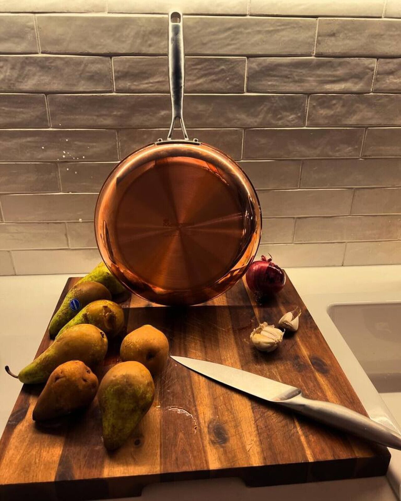 Ein Kupfertopf auf einem Holzschnittbrett mit Birnen, Knoblauch und einem Messer.