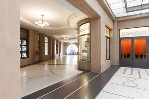 Ein geräumiger Korridor mit modernem Design, ausgestattet mit einer Glasdecke, einer Kristallleuchtre und einem Schaufenster mit dem Schriftzug 'DIVADLO'.