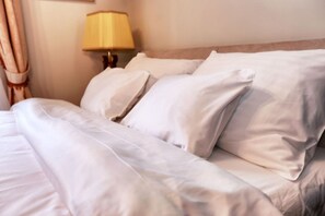 Un lit bien fait, avec du linge de lit blanc et une lampe sur une table de chevet.