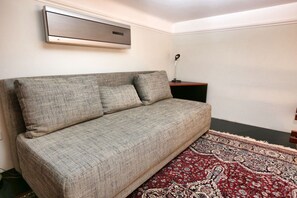 A sofa with a patterned fabric, a small side table, a wall-mounted air vent, and a patterned rug. - Classic Luxury in the Old Town (Prague 1)