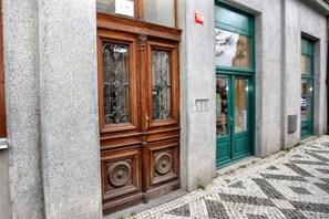 Un bâtiment doté d’une grande porte en bois ornée de motifs métalliques complexes, d’une porte verte sur la droite et d’un trottoir pavé devant l’entrée.