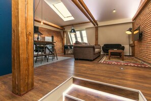 Ein Loft-Wohnraum mit freiliegenden Holzbalken, einem Essbereich mit Hockern, einer Couch und einem Couchtisch.