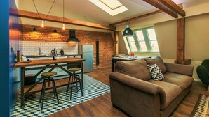 A cozy living area with a sofa, a dining table with stools, a kitchen with a brick wall, and a skylight. - Charles Bridge Loft Residence (Prague)