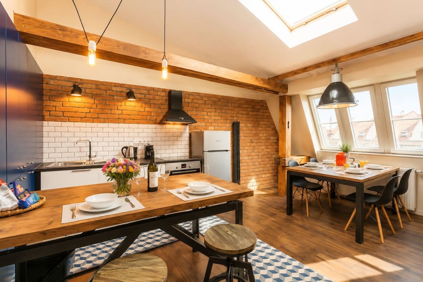 Een moderne keuken met een bakstenen muur, houten balken en een eethoek met een tafel gedekt voor twee personen.
