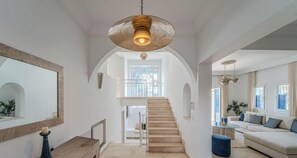 Ein großzügiger Wohnbereich mit Treppe zu einem Balkon, einem großen Spiegel und einer Hängeleuchte.