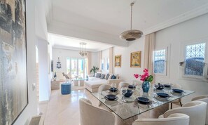 Ein geräumiger Essbereich mit einem Glastisch, weißen Sofas und Blick ins Freie.