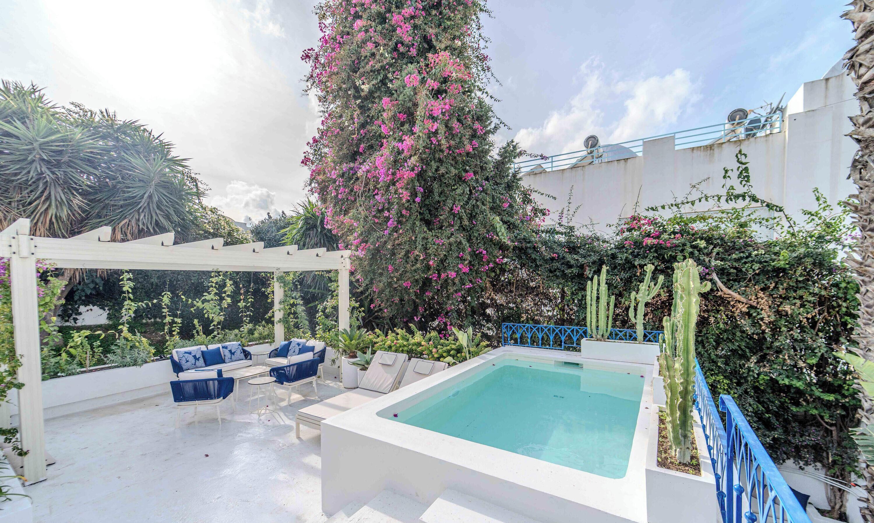 A rooftop pool area with a white pool, blue outdoor furniture, and a pergola.