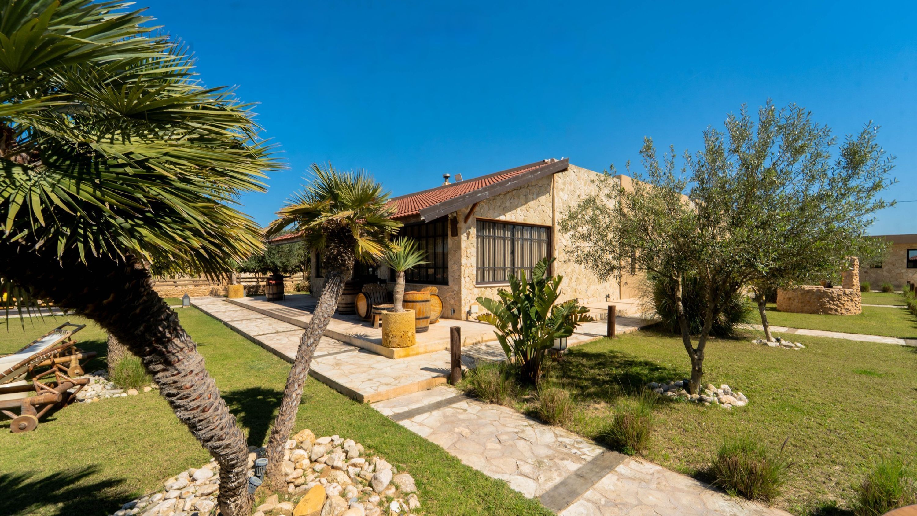 A stone building with a tiled roof, surrounded by a well-maintained lawn and palm trees.