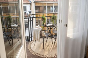 Ein Balkon mit rundem Tisch, zwei Stühlen, einer gewebten Matte und Topfpflanzen.