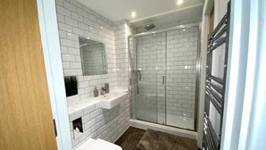 Un baño moderno con azulejos blancos tipo metro, cabina de ducha de cristal, lavamanos blanco y puerta de madera.