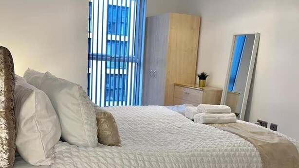 Un dormitorio con cama, armario, cómoda, espejo y ventana con persianas.