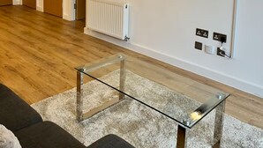 Una sala de estar con una mesa de centro de vidrio, un radiador y enchufes en la pared.