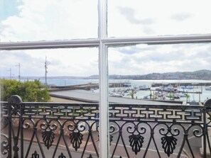 Ein Fenster mit schmiedeeisernem Gitter, Blick auf eine Marina mit Booten und eine entfernte Küstenlinie.